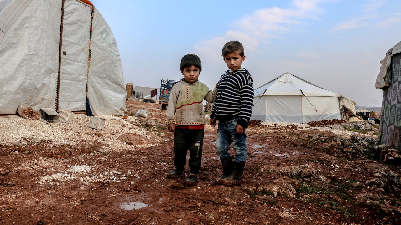 Two children standing in a muddy Syrian refugee camp in Idlib.