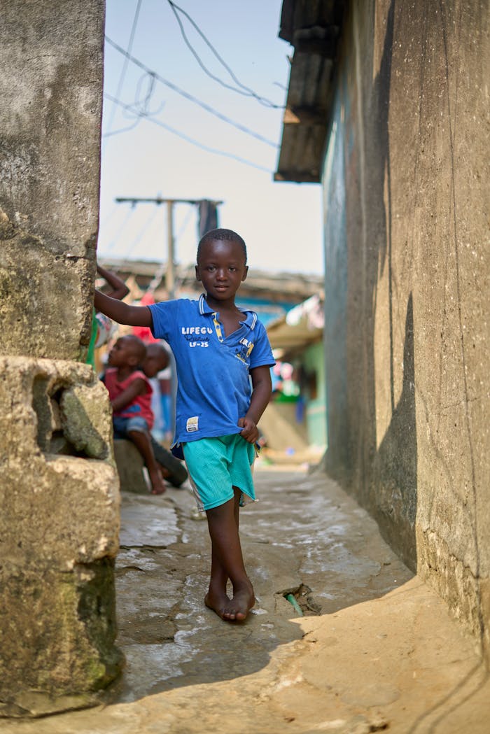 Portrait of a barefoot boy standing in a rustic village alley, showcasing simple everyday life.